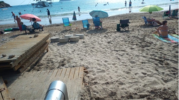 Turistas en la playa junto a la pasarela a medio reparar