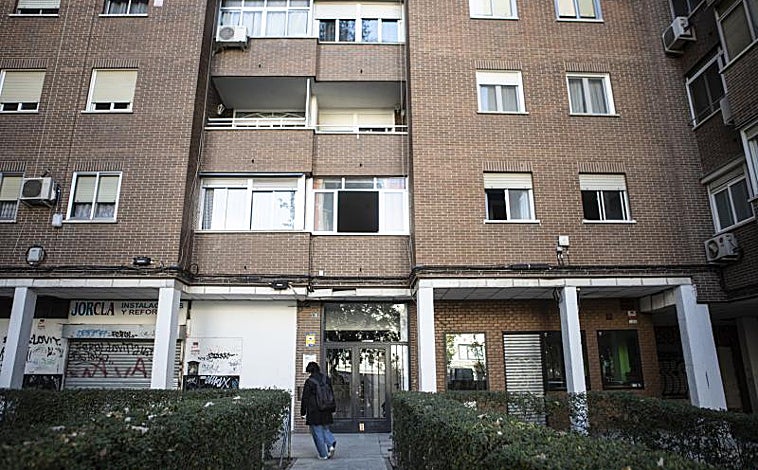 Imagen principal - Exterior del edificio en el que tuvo lugar el asesinato machista, con un ramo de flores que recuerda a las víctimas y la puerta del domicilio todavía precintada