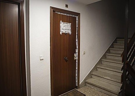 Imagen secundaria 1 - Exterior del edificio en el que tuvo lugar el asesinato machista, con un ramo de flores que recuerda a las víctimas y la puerta del domicilio todavía precintada