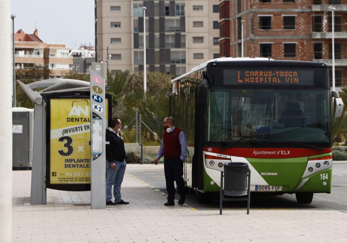 Un conductor de autobús y un viajero con mascarilla junto a una parada.