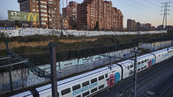 Un tren circula mientras decenas de personas observan al fondo la puesta de sol
