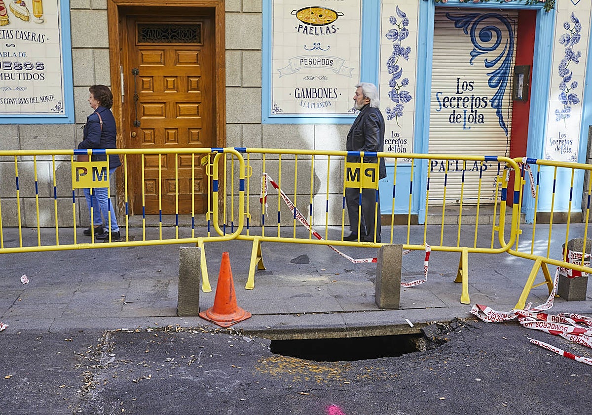 Dos personas pasan frente al socavón, a la altura del número 12