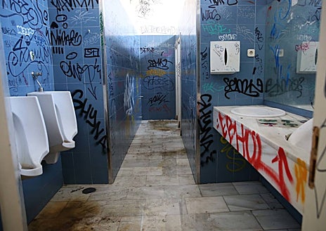 Imagen secundaria 1 - Ventanas tapiadas con ladrillos y otras con cristales rotos; e interior del colegio mayor (fotos de 2014) con imágenes de los baños y lavadoras en el momento del cierre