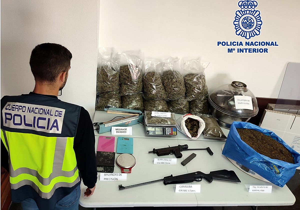Un agente de la Policía Nacional revista los cogollos y las armas intervenidas en la operación