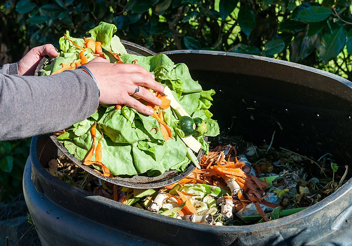 Una persona deposita restos orgánicos en un cubo de compostaje