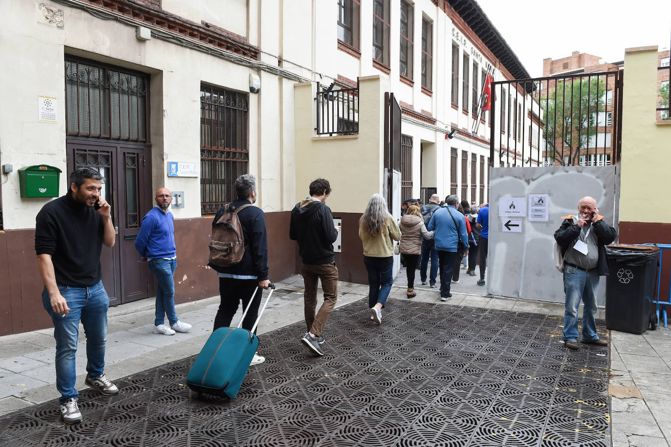 Varias personas llegan al colegio electoral CEIP Santa María, entre ellos un hombre asiste a ejercer su derecho al voto con un equipaje de viaje en Madrid 