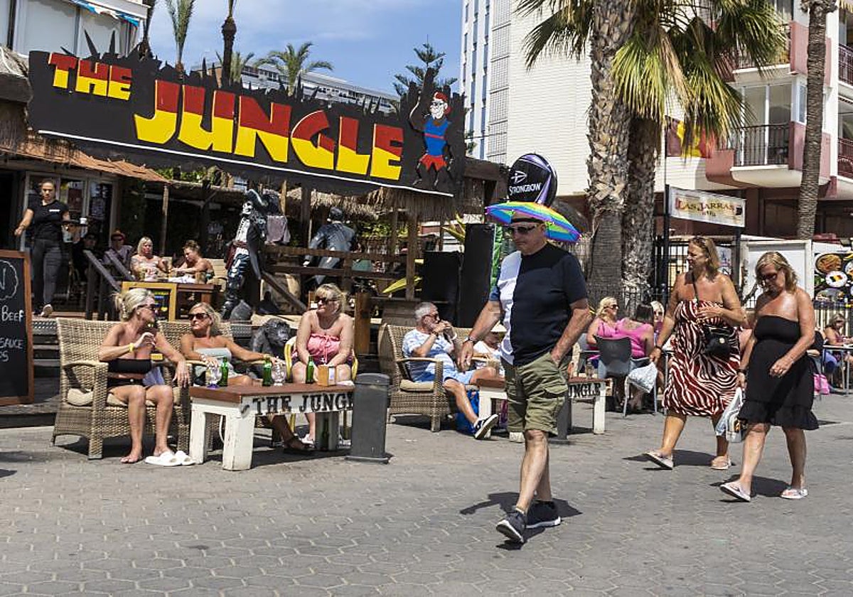 Un turista se protege del sol con un sombrero caminando junto a la playa en Benidorm.