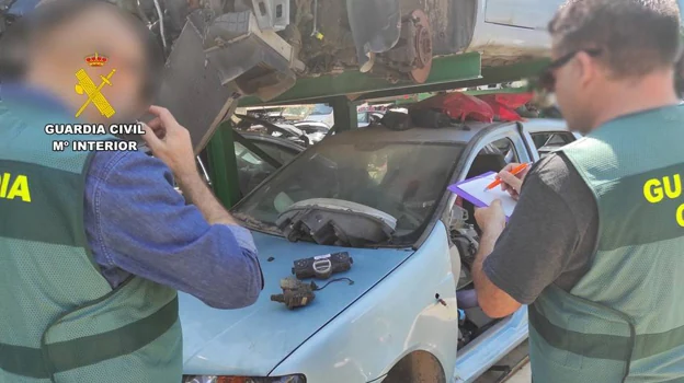 Imagen en detalle de dos agentes de la Guardia Civil frente a un coche en un desguace
