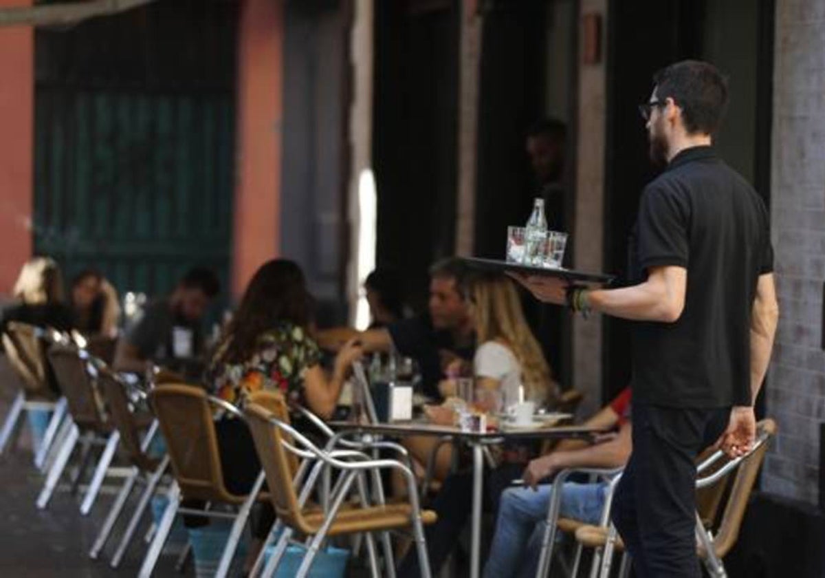 Un camarero atiende a unos clientes en unos veladores en la plaza de la Alfalfa, en Sevilla