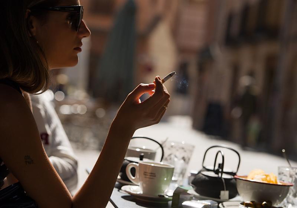 Imagen de archivo de una clienta fumando un cigarro en la terraza de un restaurante