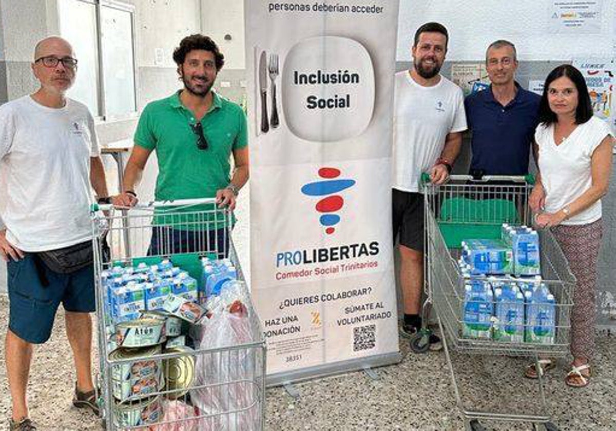 El hermano mayor de la Sentencia, de verde, junto a miembros del comedor de Trinitarios y la diputada de Caridad de la hermandad, con dos carros llenos de alimentos