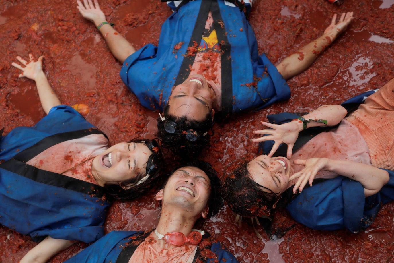 Cuatro jóvenes juegan sobre el suelo teñido de rojo en la fiesta de la Tomatina en Buñol﻿