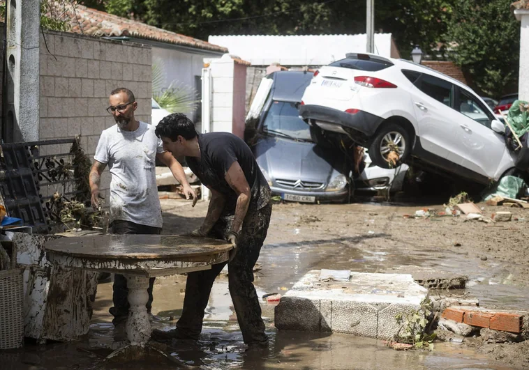 Dos vecinos de Villamanta salvan muebles;  Al fondo, los coches amontonados por la tormenta.