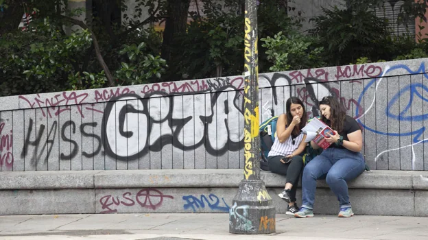 Dos jóvenes leen en uno de los muros grafitis de la Plaza del Dos de Mayo