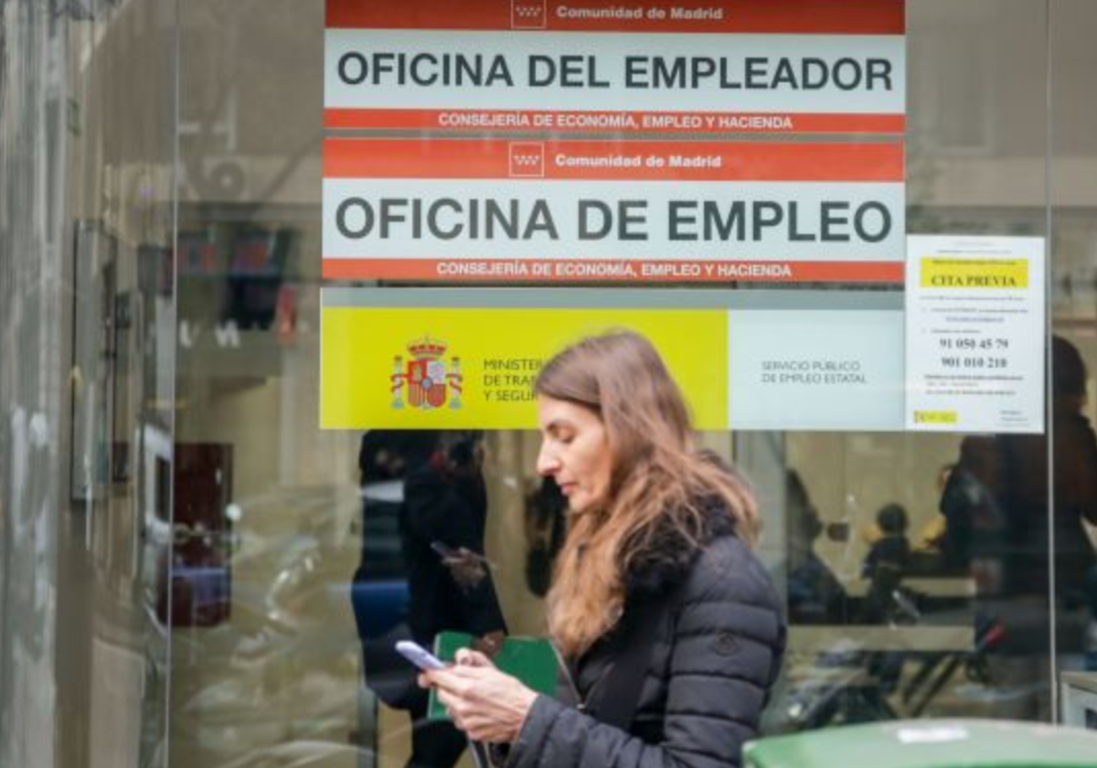 Una mujer escribe su teléfono móvil frente a una oficina de empleo en foto de archivo