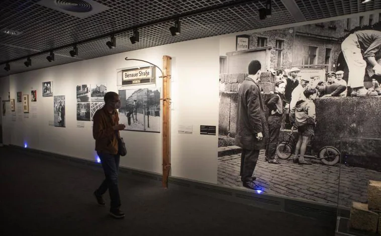 Imagen principal - Arriba, fotografías e historias de los protagonistas de la construcción del Muro.  Abajo a la izquierda, un cochecito de bebé utilizado para transportar alimentos entre ambas zonas de Berlín.  Bien, alambre de púas.