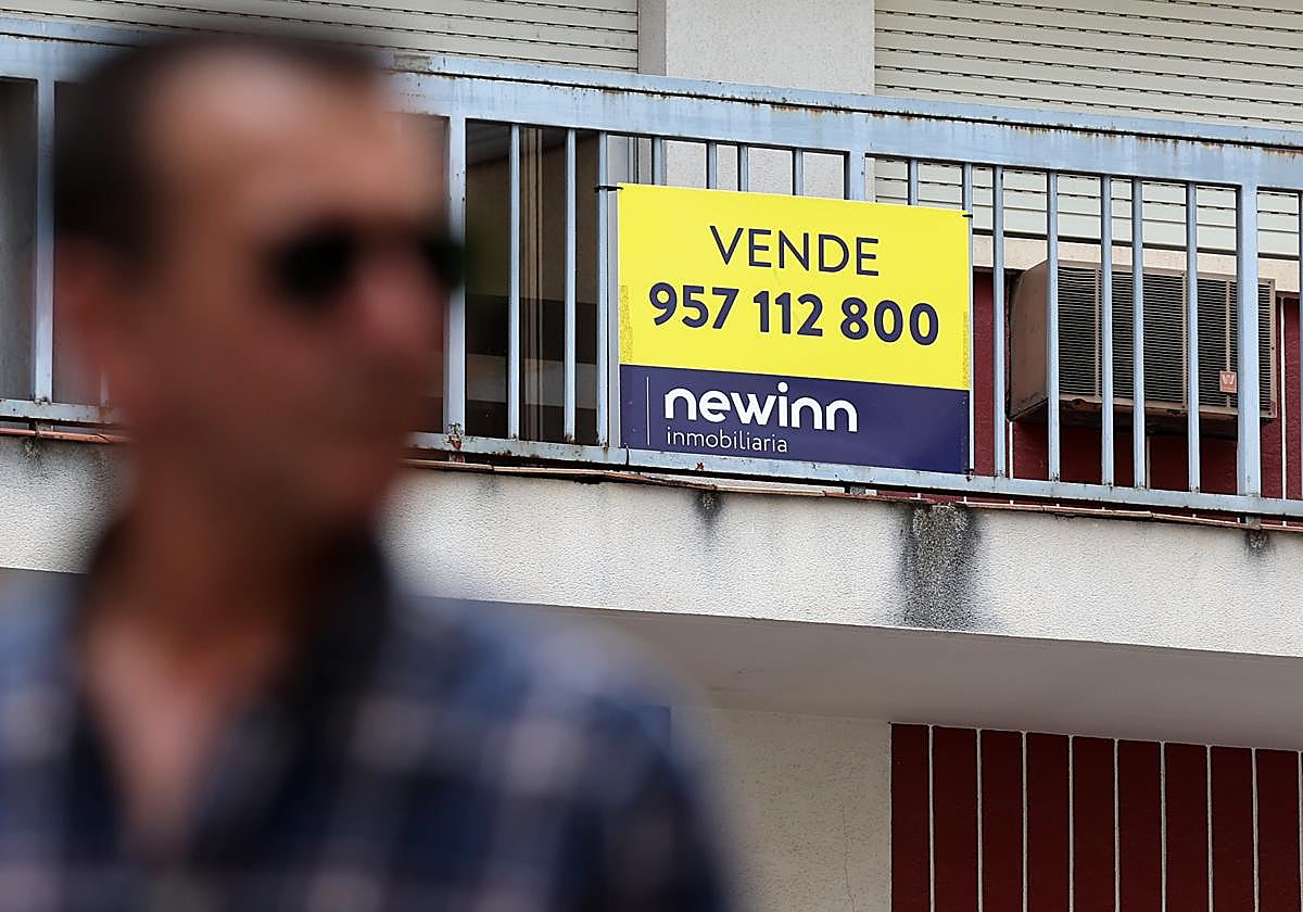Un hombre pasa delante del cartel de una vivienda en venta en Córdoba