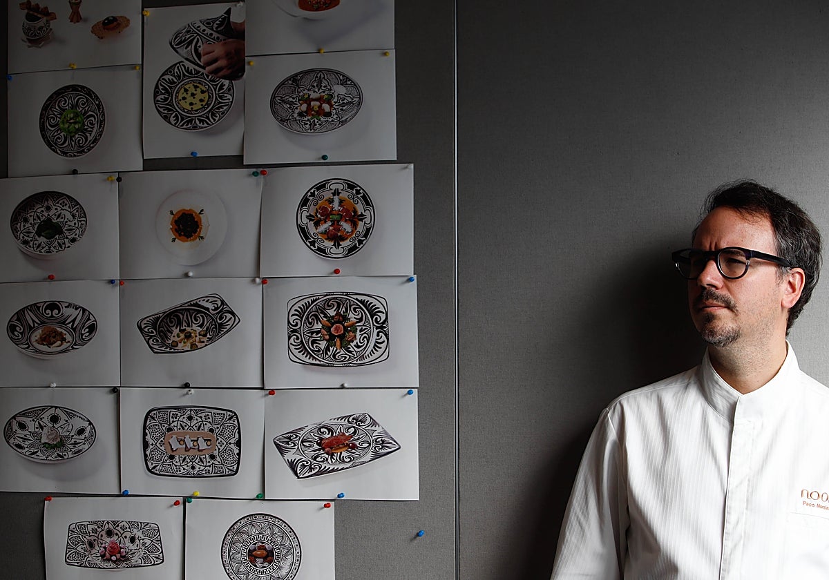 Paco Morales en la cocina del restaurante Noor junto a un mosáico de platos de su carta impresos