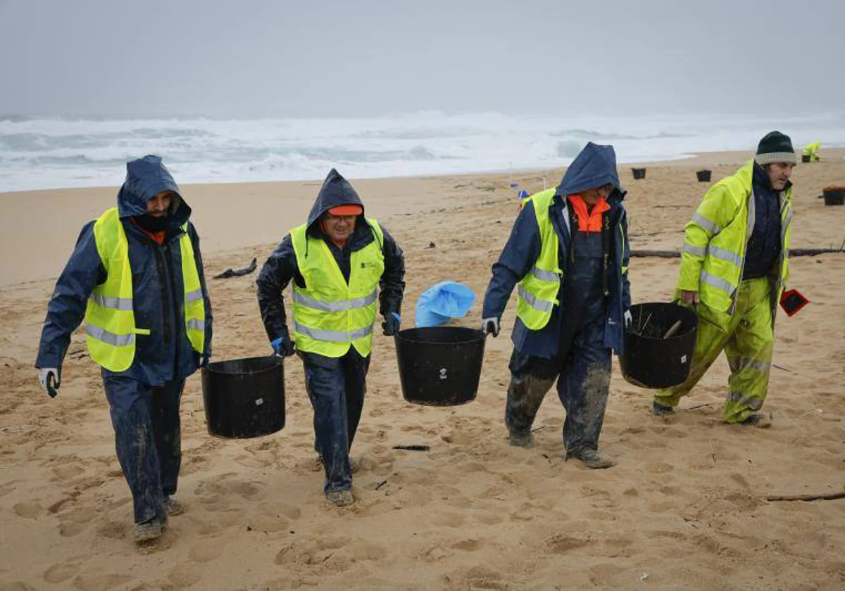 Operarios de empresas contratadas por la Xunta retiran los pellets en la playa del Vilar, en Ribeira (La Coruña)