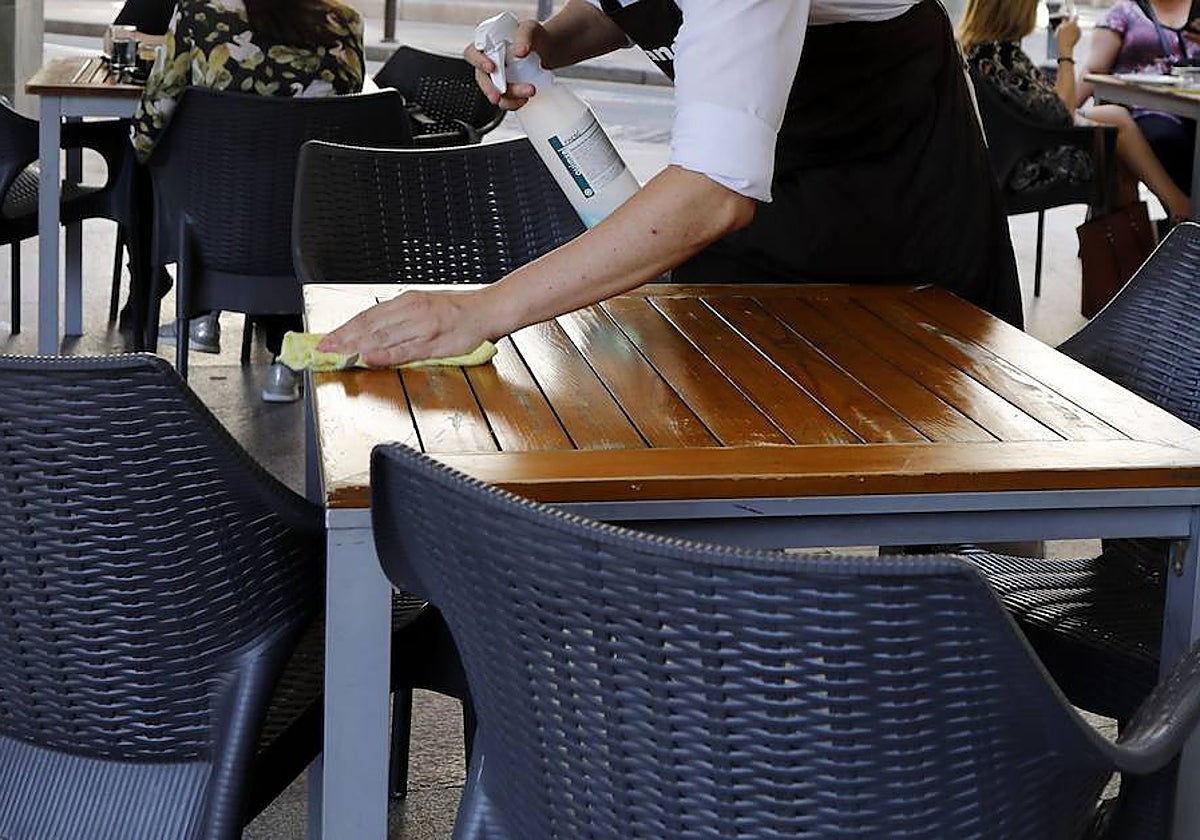 Imagen de archivo de un camarero limpiando una mesa en una terraza