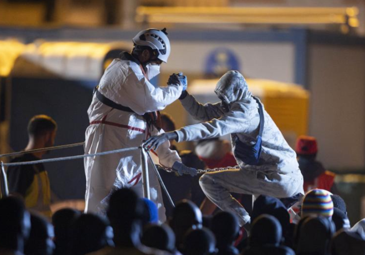 Un rescatista ayuda a su compañero a subir a la salvamar para ayudar al desembarque de migrantes en Tenerife