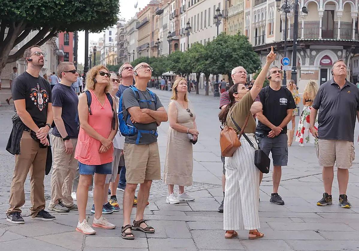Un grupo de turistas atiende las indicaciones de su guía sobre el Ayuntamiento de Sevilla
