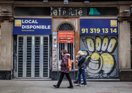 Imagen secundaria 1 - La Risueña, antaño un bar repleto de jóvenes, hoy cerrado y empapelado; en las fotos inferiores, otro local disponible para venta o alquiler en la Carrera de San Jerónimo, y una mujer pasa por delante de una espacio en desuso