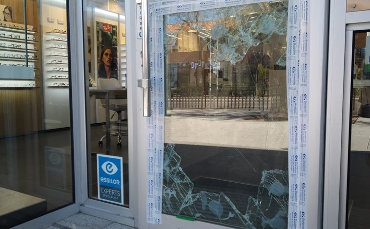 Imagen principal - Cristal reventado en la óptica y una cámara de seguridad pulverizada en la tienda de electrodomésticos, donde arracaron una de las pletinas de la puerta trasera de acceso  