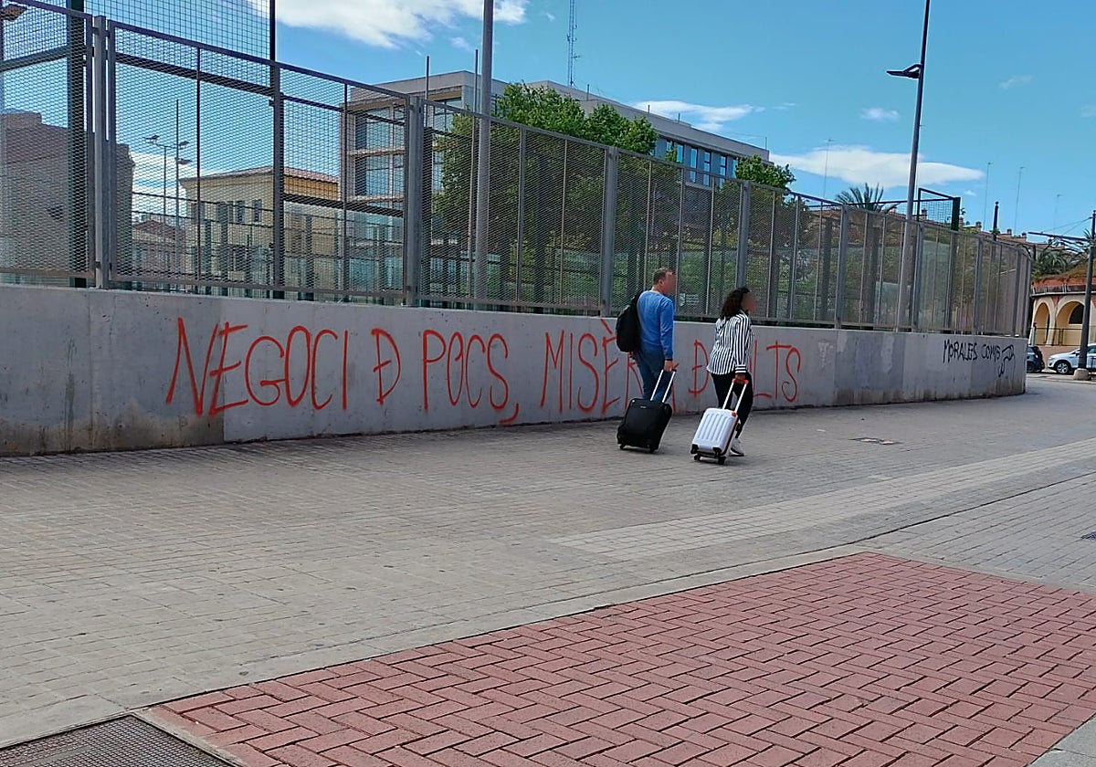 Imagen de dos turistas en el barrio del Cabanyal, en Valencia. De fondo, una pintada en la que se puede leer: 'Negocio de pocos, miseria de muchos'