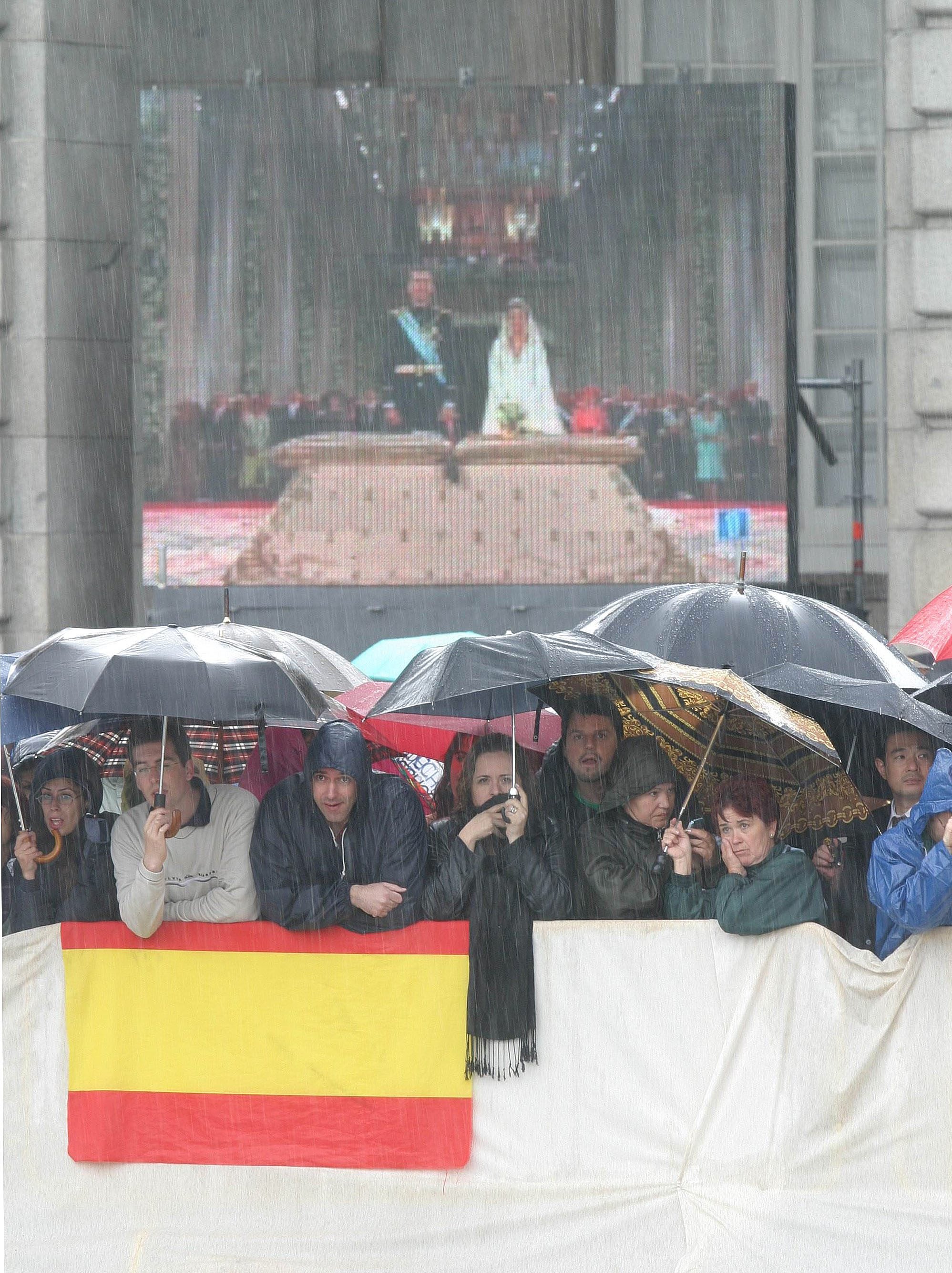 En esta imagen se puede apreciar cómo una gran pantalla, colocada en el Palacio Real, retransmite en directo la boda de los entonces Príncipes de Asturias. Muchos españoles esperaron a que los Reyes salieran de la Almudena para felicitarles y poder ver a Doña Letizia convertida, oficialmente, en Princesa de Asturias. RTVE fue la encargada de emitir en un programa especial todo el enlace real, desde las nueve de la mañana hasta las tres de la tarde. La cadena de televisión ofreció una versión en español y otra en inglés. Más de 160 operadores de los cinco continentes solicitaron la señal institucional. Se estimó una audiencia de más de mil millones de espectadores en todo el mundo. 