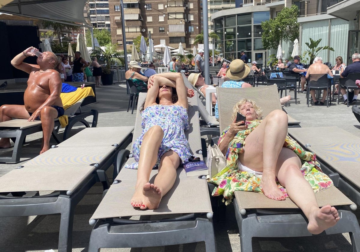 Turistas en la terraza de la piscina de un hotel en Benidorm, soportando el calor.