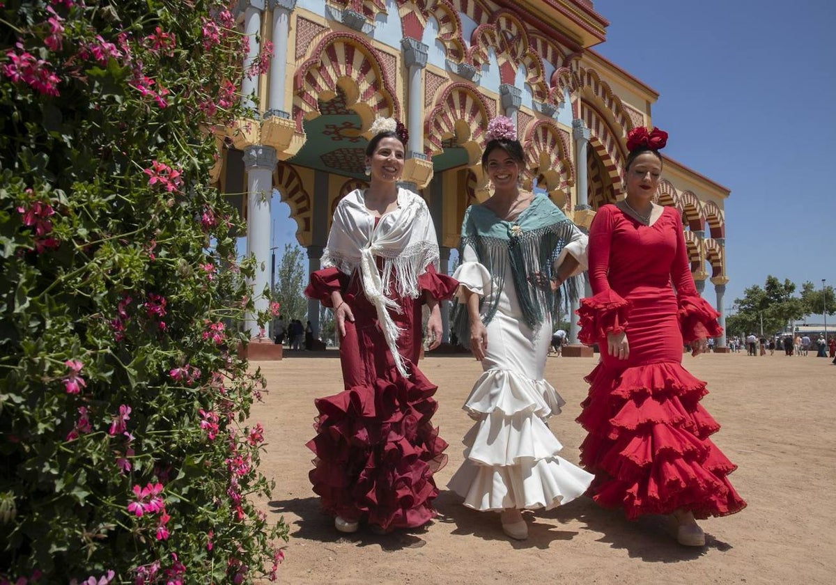 Tres mujeres vestidas de flamenca cruzan la portada en la Feria de Córdoba