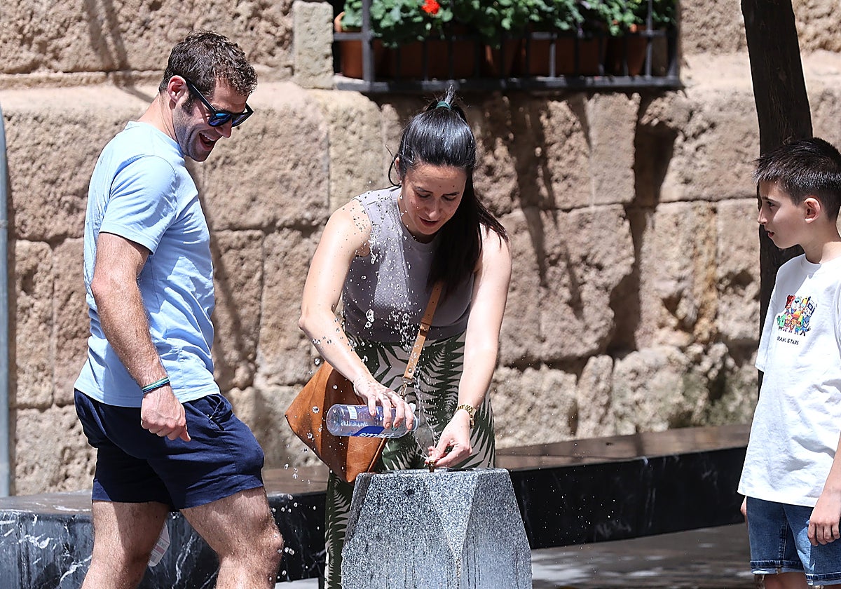 Una mujer intenta llenar su botella de agua con dos personas en pantalón corto a su lado