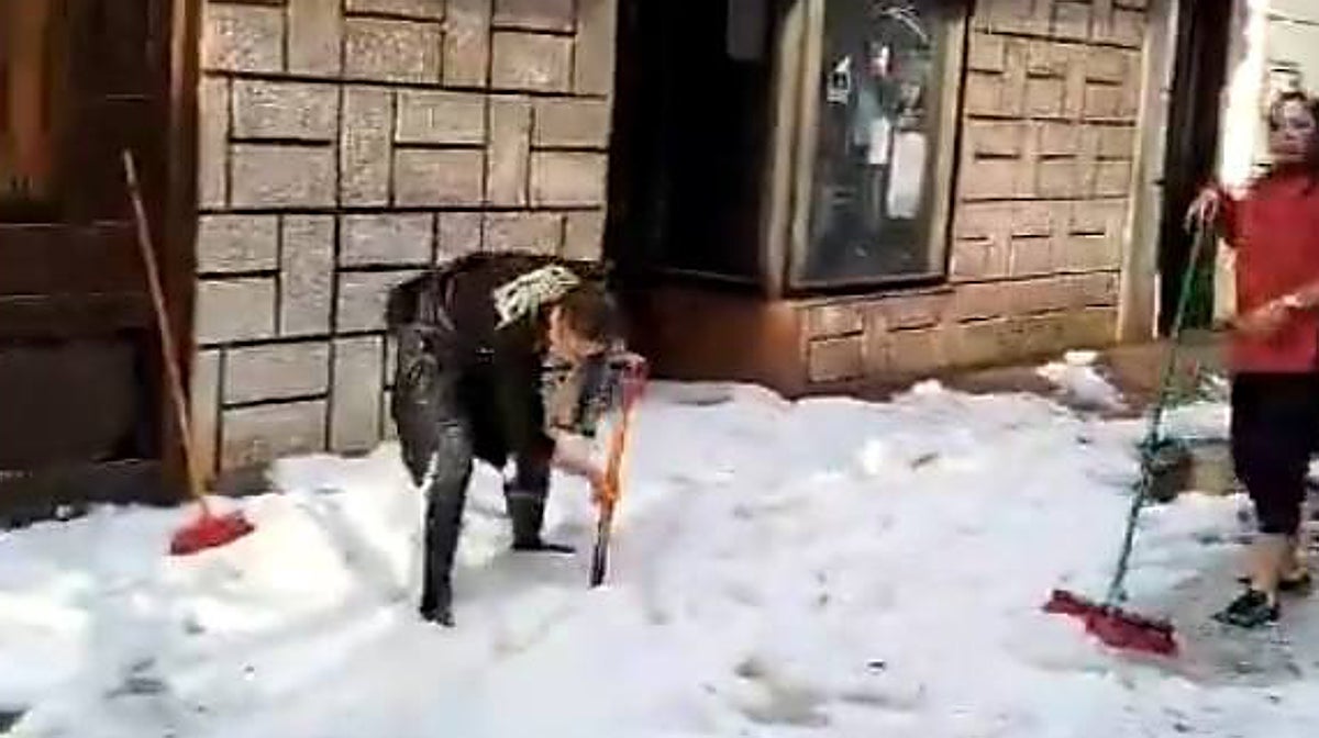 Dos mujeres limpian las calles de Cacabelos tras la espectacular granizada que cubrió de blanco las calles del municipio