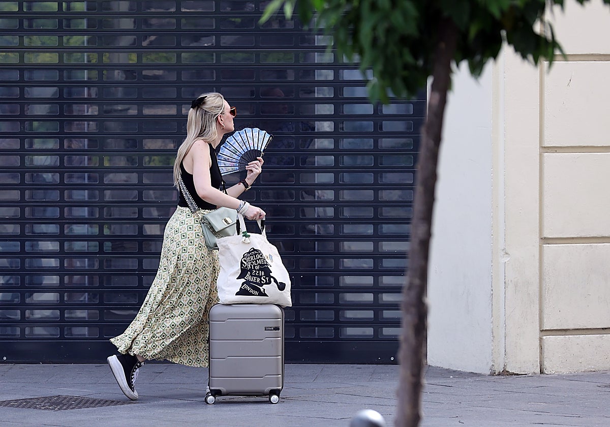 Una turista con su maleta pasa delante de una tienda cerrada en el Centro