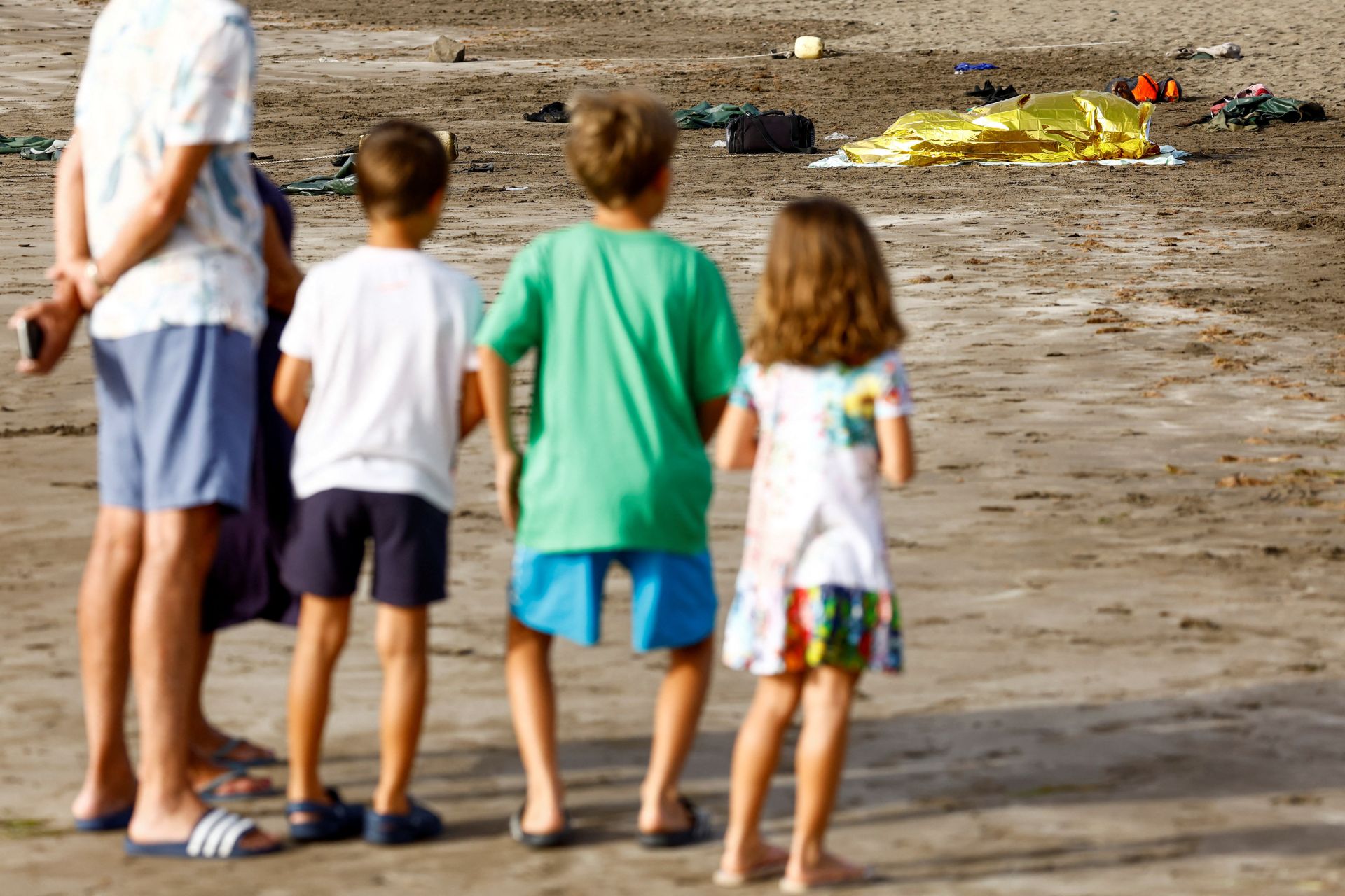 Uno de las personas que ha llegado en la embarcación tumbado en la arena ante la atenta mirada de los turistas 