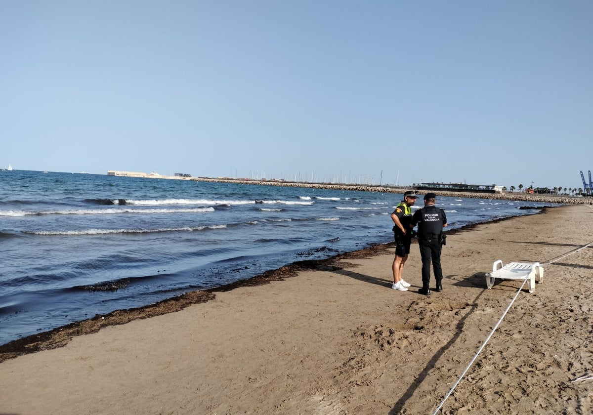 Imagen de dos agentes de la Policía Local junto a la acumulación de algas