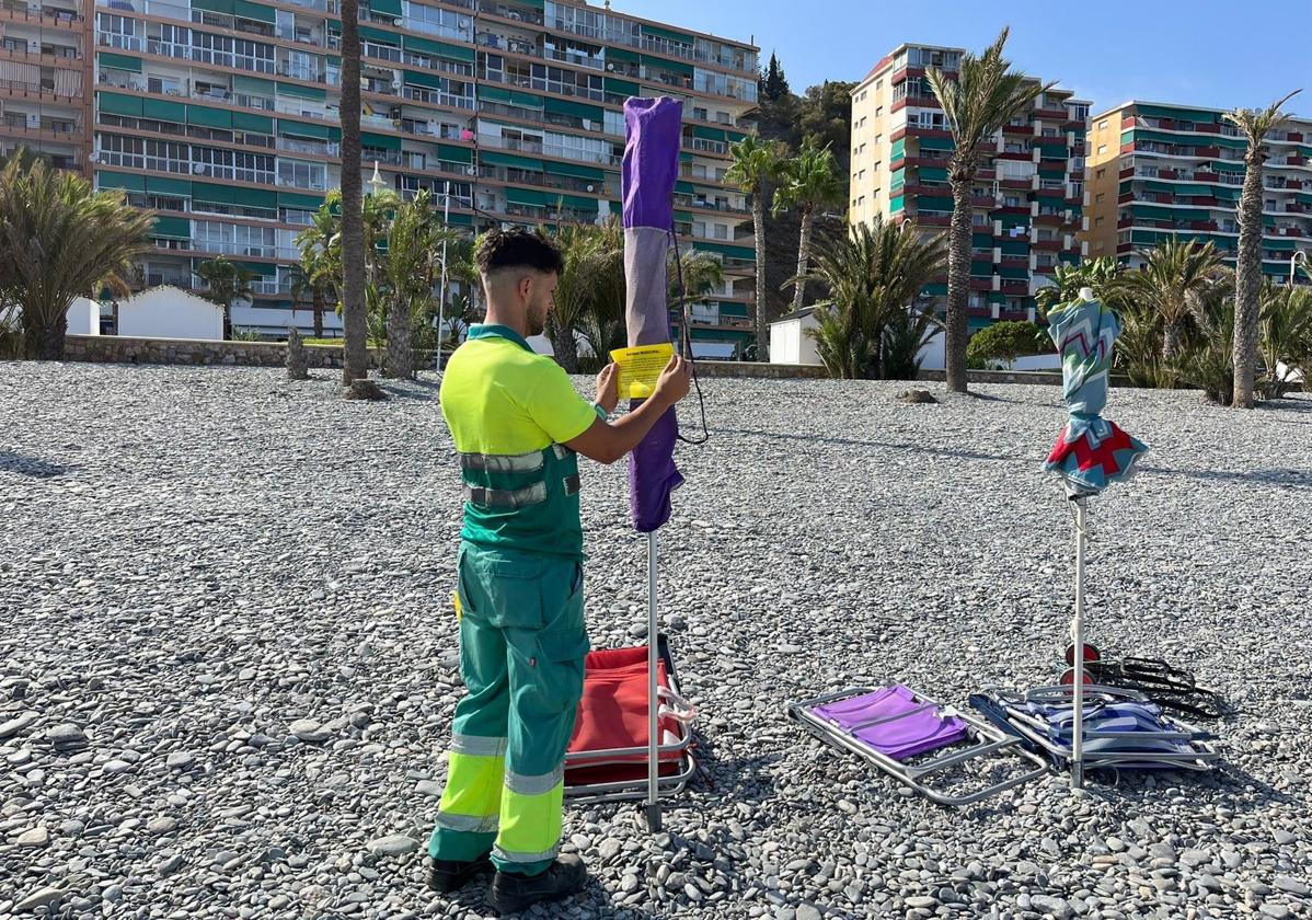 Un operario municipal colocando la pegatina disuasoria en una sombrilla en la playa de Motril