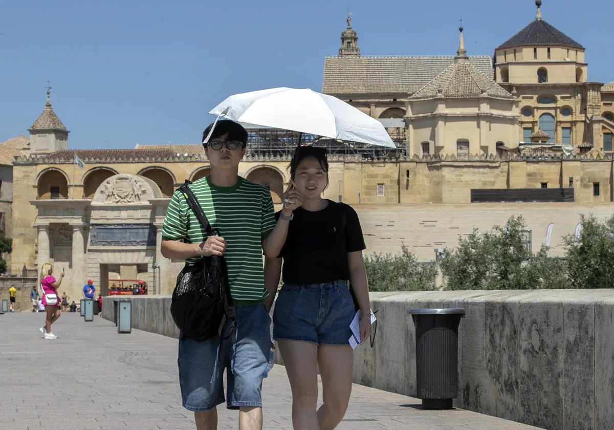 Una pareja de turistas japoneses se protege del sol mientas pasea por el Puente Romano