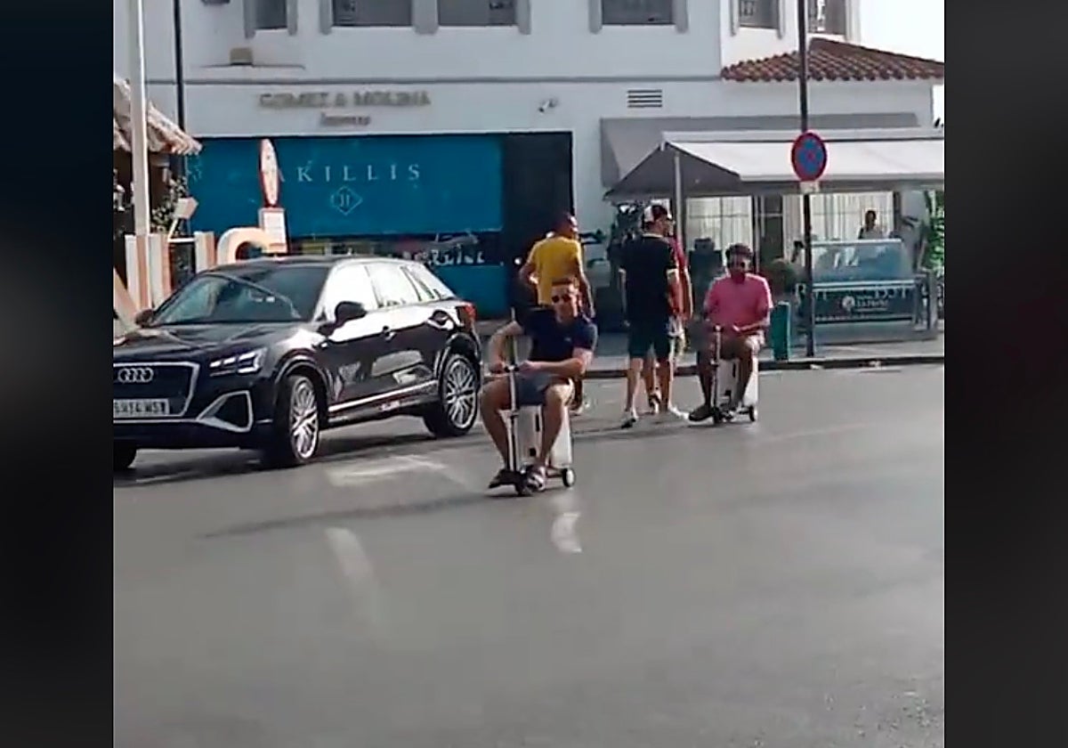 Dos turistas se desplazan en el patinete-maleta por Puerto Banús, en Marbella