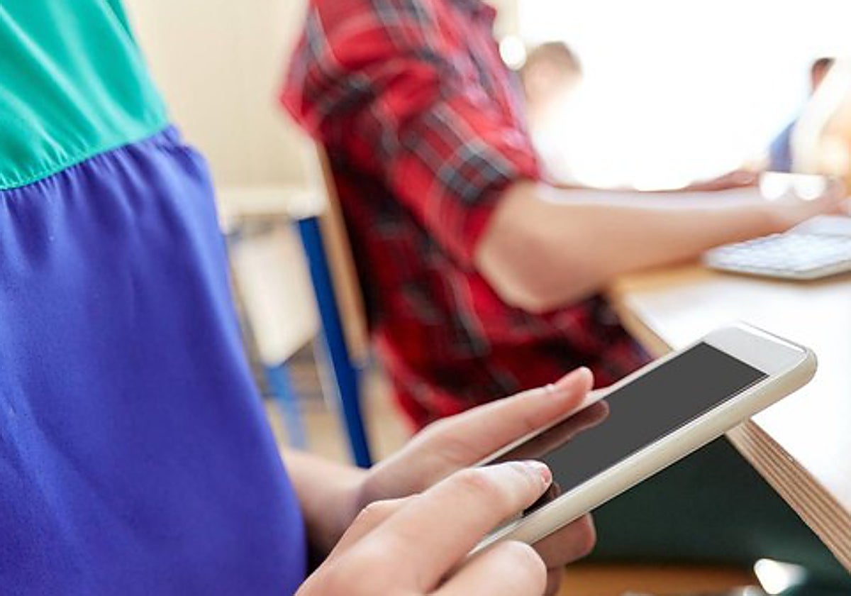 Un menor con un teléfono móvil en un aula
