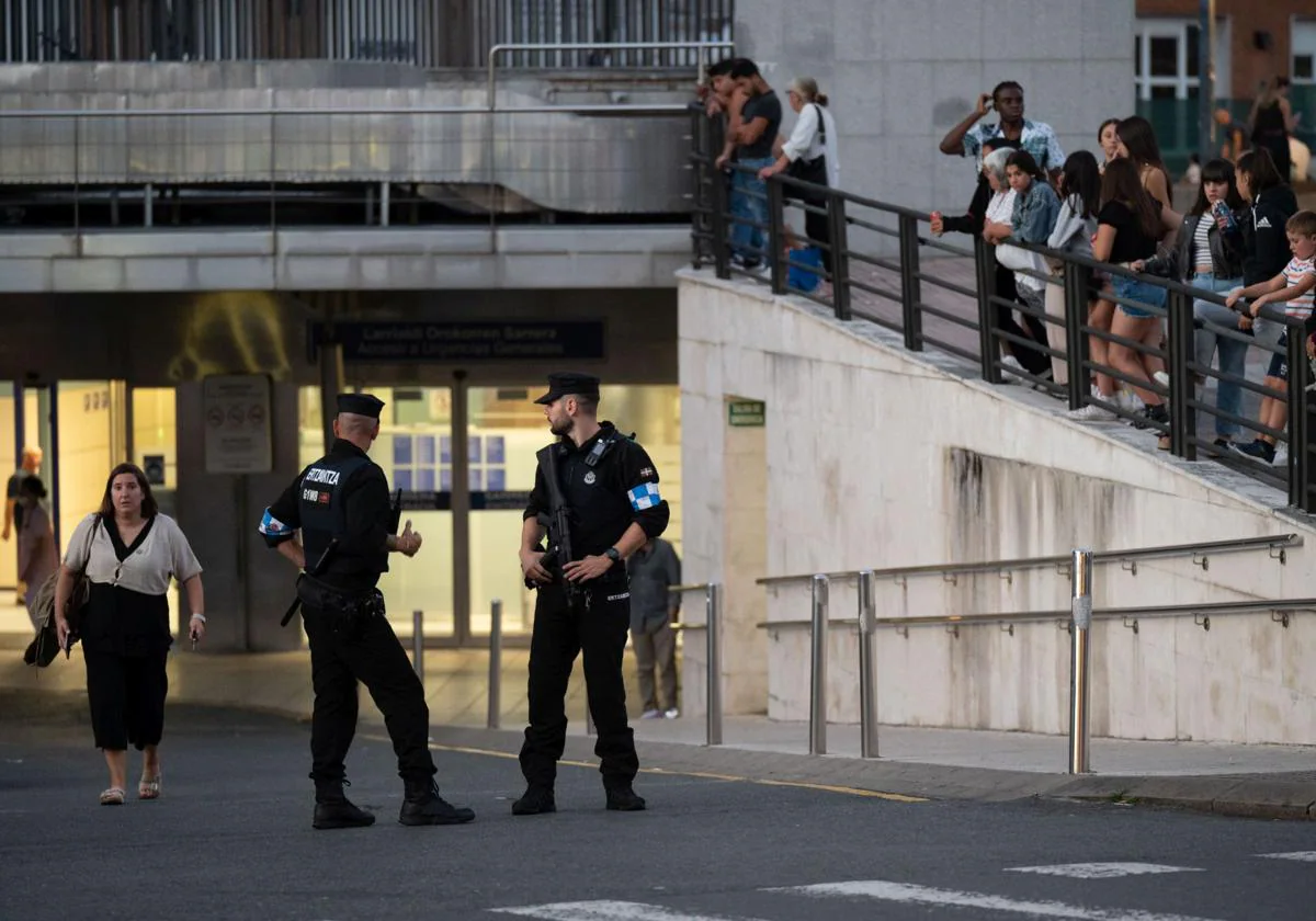 Una pareja de la Ertzaintza vigila la entrada al Hospital de las Cruces con varias personas esperando la salida de varias personas