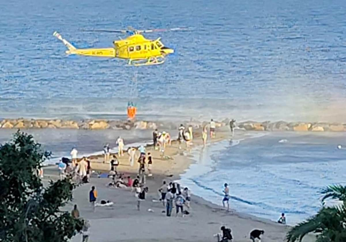 El helicóptero en el momento de hacer una recarga de agua en la playa del Postiguet, junto al Castillo de Santa Bárbara, por el incendio