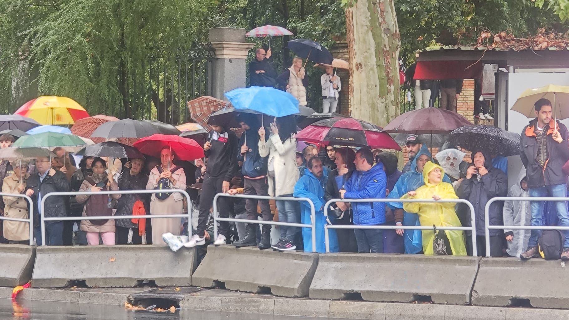 Decenas de espectadores, con chubasqueros y paraguas, esperando el inicio del desfile, a pesar de la intensa lluvia