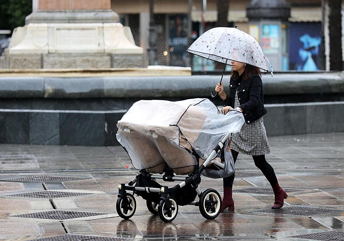 Una mujer con un carrito bajo la lluvia paseando por las Tendillas