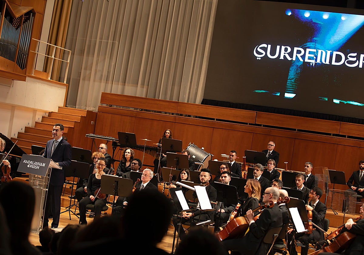 Moreno habla delante de la Orquesta Ciudad de Granada y la pantalla donde se proyectó el spot