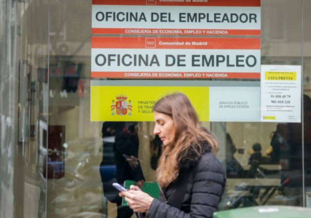 Una mujer escribe en su teléfono móvil frente a una oficina de empleo en foto de archivo