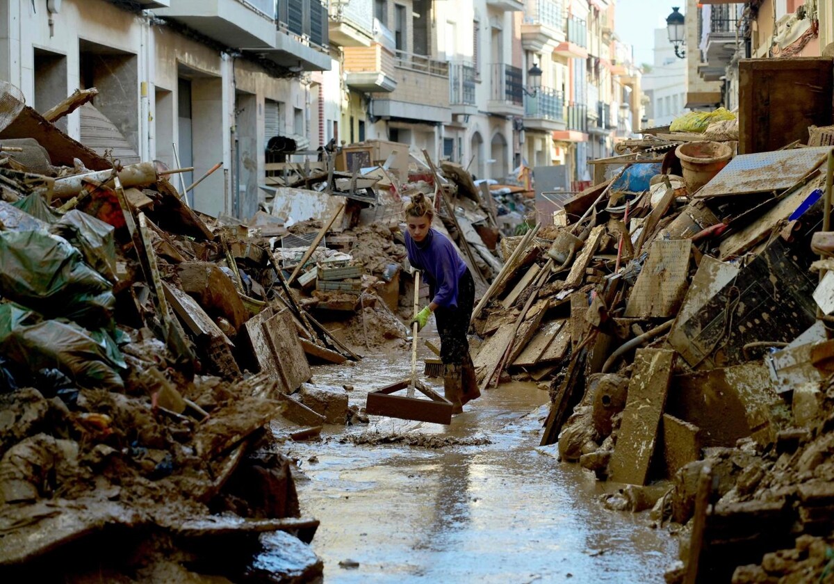 Una vecina intenta quitar el lodo en su calle, en Paiporta