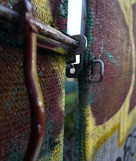 Imagen secundaria 2 - Arriba, el pabellón con una tela de protección desde que se paralizó su derrumbe. Abajo, izq, restos de basura de los asentados en el solar. Dcha, el candado instalado