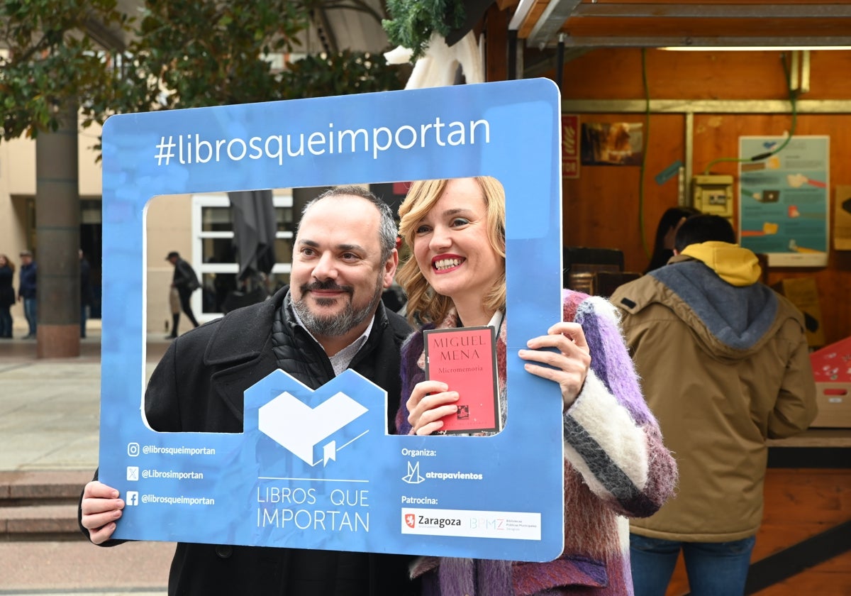 Pilar Alegría con Jorge Gonzalvo, de la ONG Atrapavientos, en la iniciativa 'Libros que importan', que cumple este año su octava edición en una caseta del mercadillo navideño de la plaza del Pilar